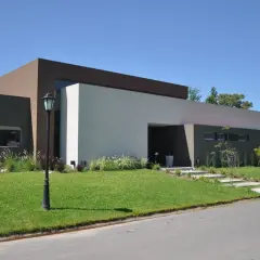 Casa moderna con pintadas color de casa afuera, en tonos tierra y blanco. Jardín verde y cielo azul.