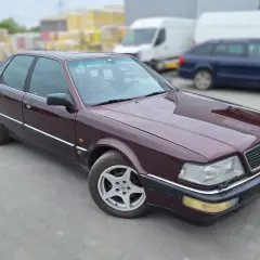 Bordowy Audi V8 z lat 90. na parkingu, w tle białe vany i niebieski kombi.