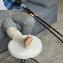 Osoba z zabandażowaną nogą i kulami obok, zastanawia się nad stopniem skręcenia stawu skokowego ile procent.