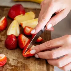 Hände schneiden Erdbeeren und Äpfel auf einem Holzbrett. Diese Früchte sind reich an Flavonoiden, die gut für die Gesundheit sind.