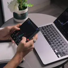 Analityk sprawdza wykresy na telefonie i laptopie, analizując dane finansowe.