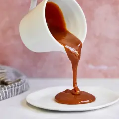 Flüssige Karamellsauce fließt aus einer weißen Kanne auf einen Teller. Ein einfaches karamellsauce rezept für süße Momente.
