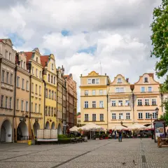Kolorowe kamienice na jeleniogórskim rynku, z arkadami i kawiarnianymi ogródkami, pod błękitnym niebem.