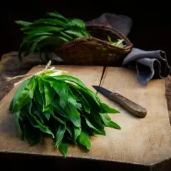 Un bouquet d'ail des ours fraîchement cueilli, prêt pour une recette. Un couteau repose sur la planche à découper en bois.