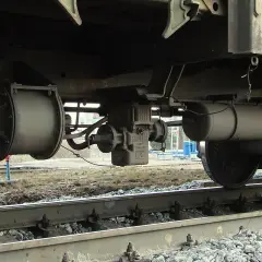 Podwozie wagonu z widocznymi elementami pneumatycznych hamulców kolejowych, w tym zbiornikiem powietrza i zaworem.