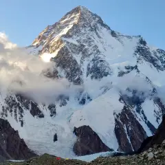 Majestatyczny K2, najwyższy szczyt Karakorum, wyłania się z chmur. Słońce oświetla jego śnieżne zbocza, ukazując surowe piękno gór.