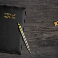 Czarny notatnik z napisem "INTENCJE MSZALNE", długopis i złoty krzyż. Zastanawiasz się, ile kosztuje msza gregoriańska w Niepokalanowie?