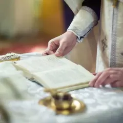 Dłoń duchownego trzyma księgę, czytając tekst. To może być fragment o tym, czym jest rezurekcja.