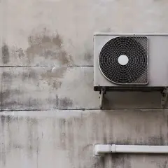 Unité extérieure d'une pompe à chaleur fixée à un mur en béton. Vérifiez l'éligibilité pompe à chaleur gouvernement pour des aides.