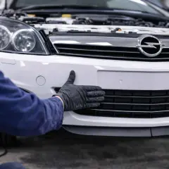 Ręka w czarnej rękawiczce sprawdza zderzak OPC Astra H.