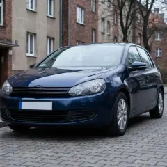 Ciemnoniebieski samochód stoi na ulicy z kostki brukowej. Brak tablic rejestracyjnych, co sugeruje rejestracja samochodu bez tablic.