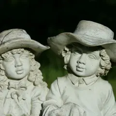 Zwei alte Gartenfiguren aus Stein, Kinder mit Hüten, im Grünen.