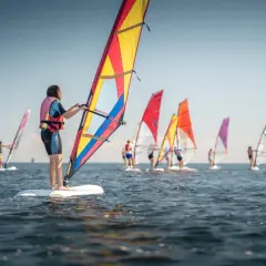 Ludzie na deskach z żaglami, uczący się, co to windsurfing. Wesoła grupa na wodzie w słoneczny dzień.