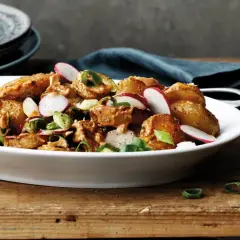 En härlig rostad potatissallad med rädisor och salladslök, serverad i en vit skål på ett träbord.
