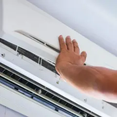 Mano revisando un aire acondicionado con 20 años de servicio, mostrando las rejillas y el interior.