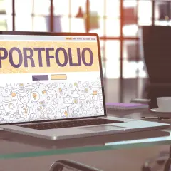 Laptop z napisem "PORTFOLIO" i rysunkami symbolizującymi pracę kreatywną. To świetny przykład, portfolio co to jest.