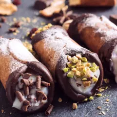 Trzy pyszne cannoli z kremem, posypane cukrem pudrem, pistacjami i czekoladą. Idealne na deser, gdy szukasz inspiracji na cannoli przepis.