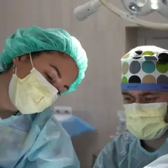 Pielęgniarka i chirurg w maseczkach i czepkach pracują pod lampą operacyjną.