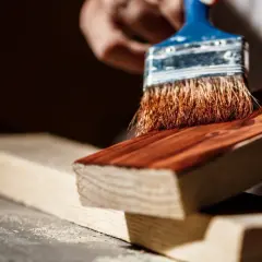 Pędzel nakłada lakier jachtowy na drewno. Zastanawiasz się, jak długo schnie lakier jachtowy? Czas schnięcia zależy od wielu czynników.