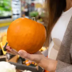 Mano che tiene una zucca Delica arancione, pronta per essere cucinata.