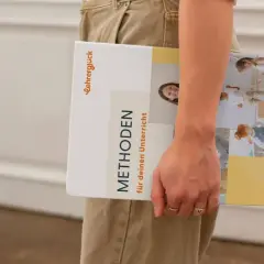 Ein Buch mit dem Titel "Methoden für deinen Unterricht" wird von einer Person gehalten. Es zeigt Bilder von Kindern in einer Lernumgebung.