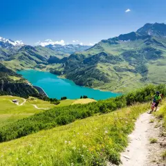 Une personne fait une rando alpes, profitant d'un lac turquoise et de montagnes majestueuses.
