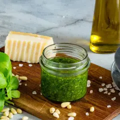 Słoiczek domowego pesto z bazylii, idealny sposób, jak zrobić pesto z bazylii na zimę. Obok świeża bazylia, orzeszki piniowe, parmezan i oliwa.
