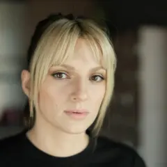 Portret młodej kobiety z blond grzywką i ciemnymi pasemkami włosów, patrzącej w obiektyw.