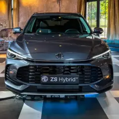 Szary MG ZS Hybrid+ prezentuje się elegancko na tle wnętrza z zasłonami i krzesłami.