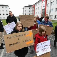 Ludzie protestują pod blokami, trzymając transparenty. Jeden z nich głosi "Mieszkania Plus, a jednak minus".