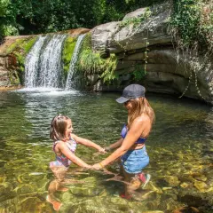 Madre e hija disfrutan de unas refrescantes piscinas naturales con una cascada al fondo.