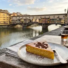 Ein Stück Schiacciata alla Fiorentina mit Kakaopulver-Dekor, serviert am Arno mit dem Ponte Vecchio im Hintergrund.