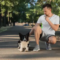 Mężczyzna w parku dmucha w gwizdek dla psa, ćwicząc posłuszeństwo.