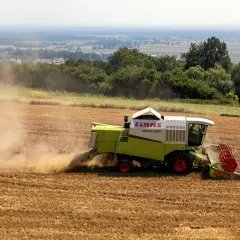 Kombajn zbożowy CLAAS Mega 350 zbiera plony na polu. Dymiące maszyny rolnicze to symbol ciężkiej pracy, która dzięki płatnościom bezpośrednim staje się bardziej opłacalna.