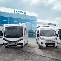 Una caravana y tres autocaravanas KNAUS blancas frente a un edificio moderno.