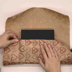 Händer viker hjärtmönstrat papper runt ett svart paket. Snart är det dags att slå in stort paket.