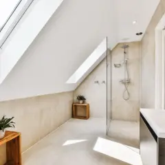 Élégante salle de bain sous comble avec douche moderne, lavabo design et puits de lumière.