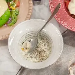 En skål med krämig majs, kryddad med peppar, bredvid en tallrik med grönsaker och en rosa tallrik med jordgubbar och grädde.