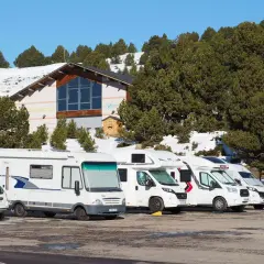 Stationnement de camping-cars dans une aire de camping car Andorre, avec un bâtiment et des pins enneigés en arrière-plan.