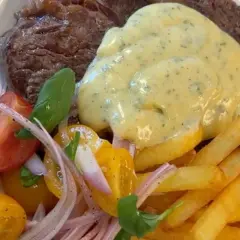 En saftig biff med krämig bearnaisesås, gyllene pommes frites och en fräsch tomatsallad. En klassisk steak frites-upplevelse.
