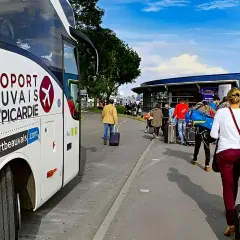 Autobus z napisem "AÉROPORT BEAUVAIS OISE/PICARDIE" czeka na pasażerów z walizkami przed terminalem.