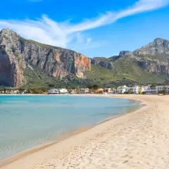 Spiaggia di San Vito Lo Capo, Sicilia, con acque turchesi e montagne imponenti sullo sfondo. Un paradiso per chi ama il mare.
