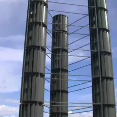 Trzy wysokie, pionowe turbiny wiatrowe, polskie innowacje w energetyce odnawialnej, na tle błękitnego nieba z chmurami.