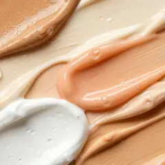 Texturen von cremiger weißer, pfirsichfarbener und beiger Feuchtigkeitscreme mit glänzenden Tropfen.