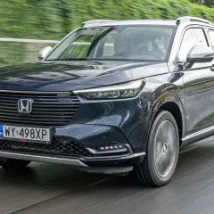 Ciemnogranatowy Honda HR-V na mokrej drodze. Nowoczesne reflektory i grill podkreślają jego dynamiczny charakter. Silniki tej generacji zapewniają oszczędność i płynność jazdy.