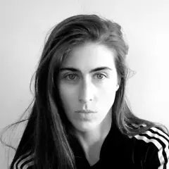 Ritratto in bianco e nero di Mara Oscar Cassiani, con lunghi capelli castani e indosso una felpa con le iconiche tre strisce.