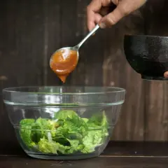 Eine Löffelspitze mit köstlichem Salatdressing tropft in eine Schüssel mit frischem Salat.
