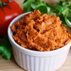 Pyszna, domowa pasta z soczewicy w białej miseczce, obok pomidora i świeżej zieleniny. Idealna na kanapki.