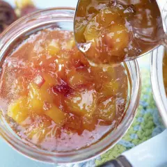 Ein Löffel voller glänzender Nektarinen Marmelade wird über ein Glas voller Fruchtstücke geschöpft.