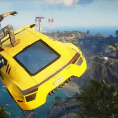 Rico z Just Cause 5 skacze z żółtego supersamochodu nad klifem, w tle widać śródziemnomorską wioskę i morze.